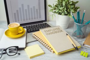 Desk with open laptop coffee and employee handbook