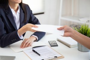 Close up of woman handing over a check to an employee at her desk