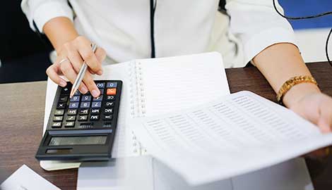 Close up of woman typing on a calculator while reviewing a document