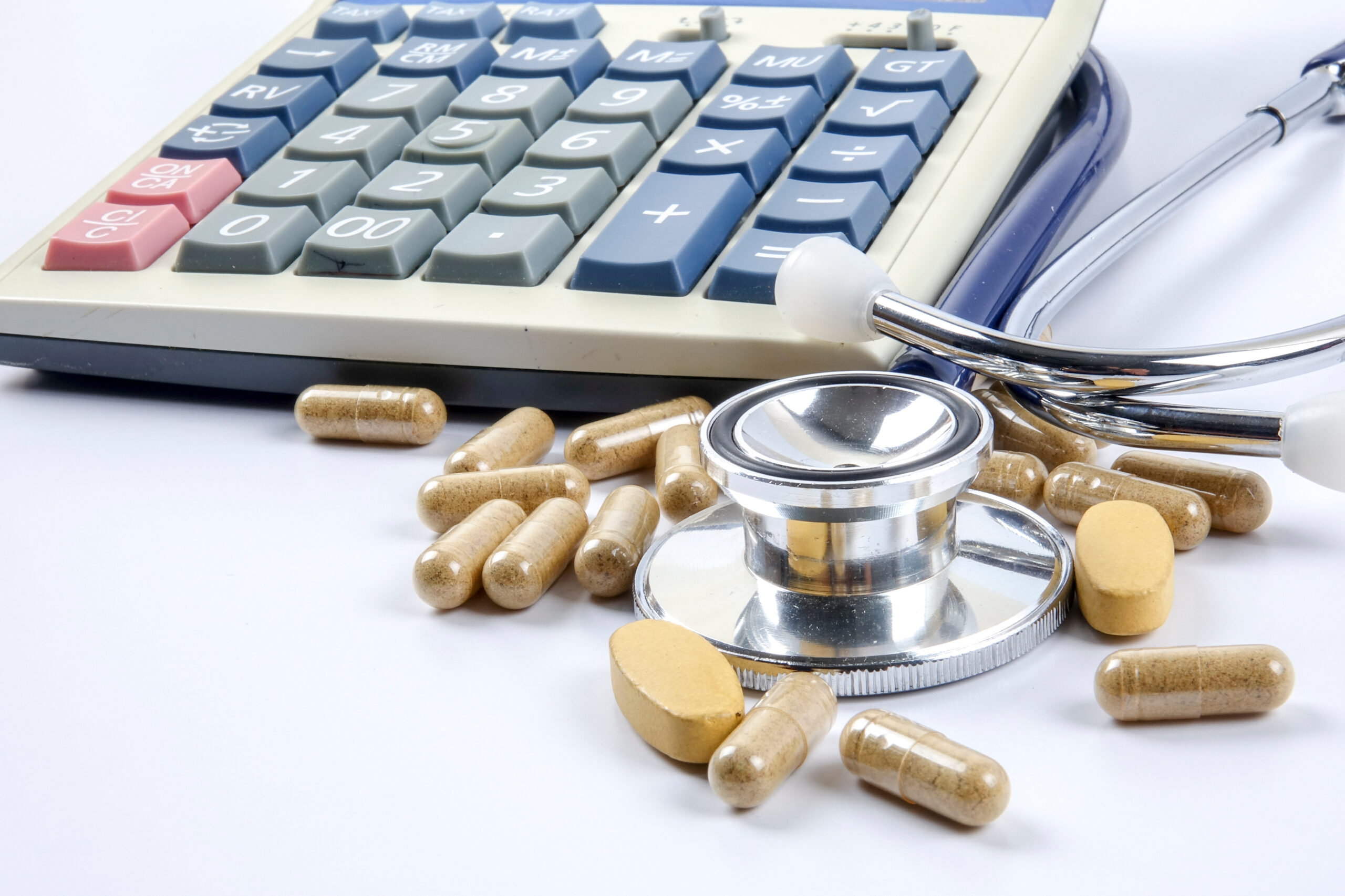 A calculator with a stethoscope and pills scattered around it.